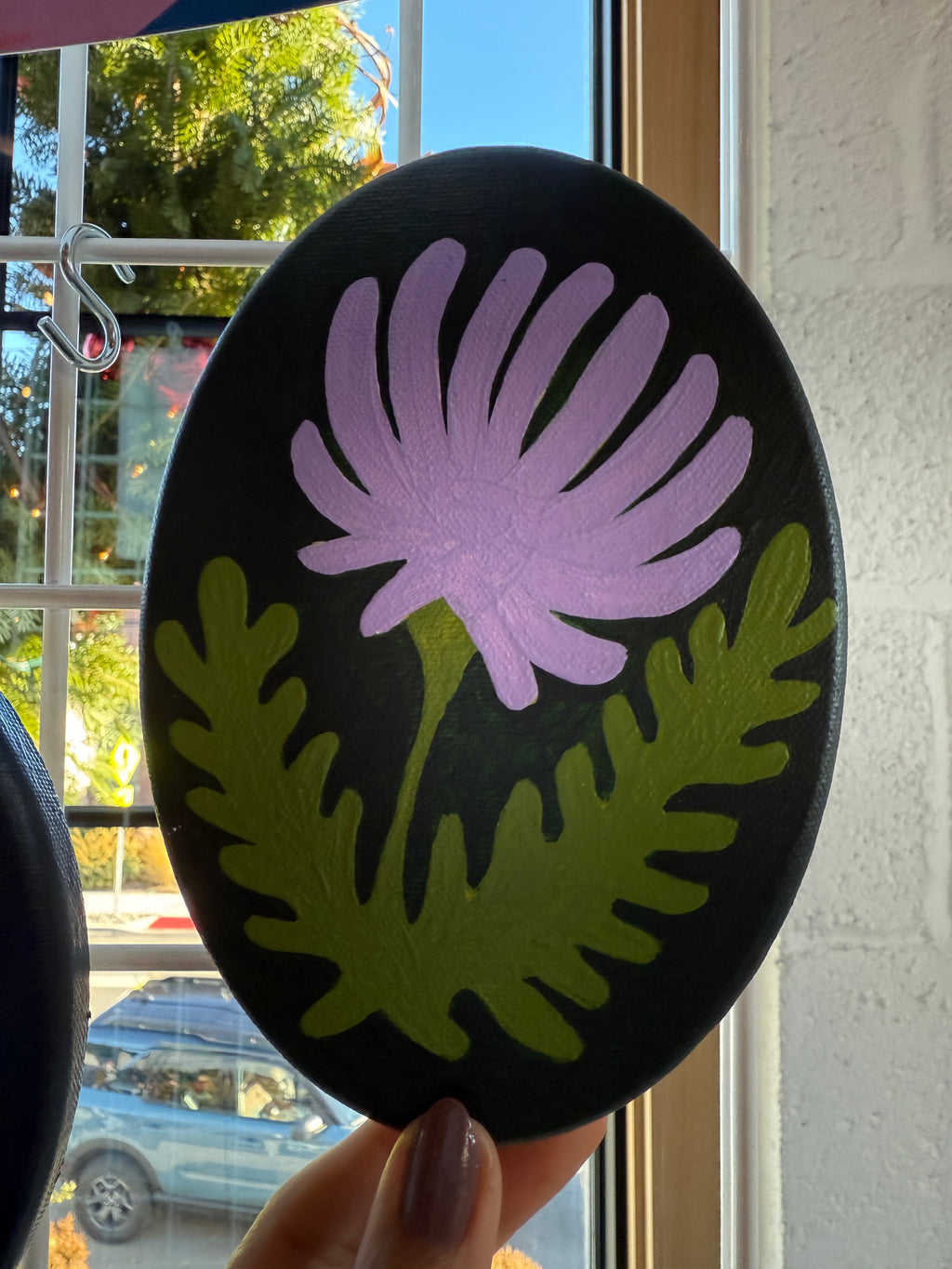 Round black coaster with purple flower and green leaves design held by a hand.