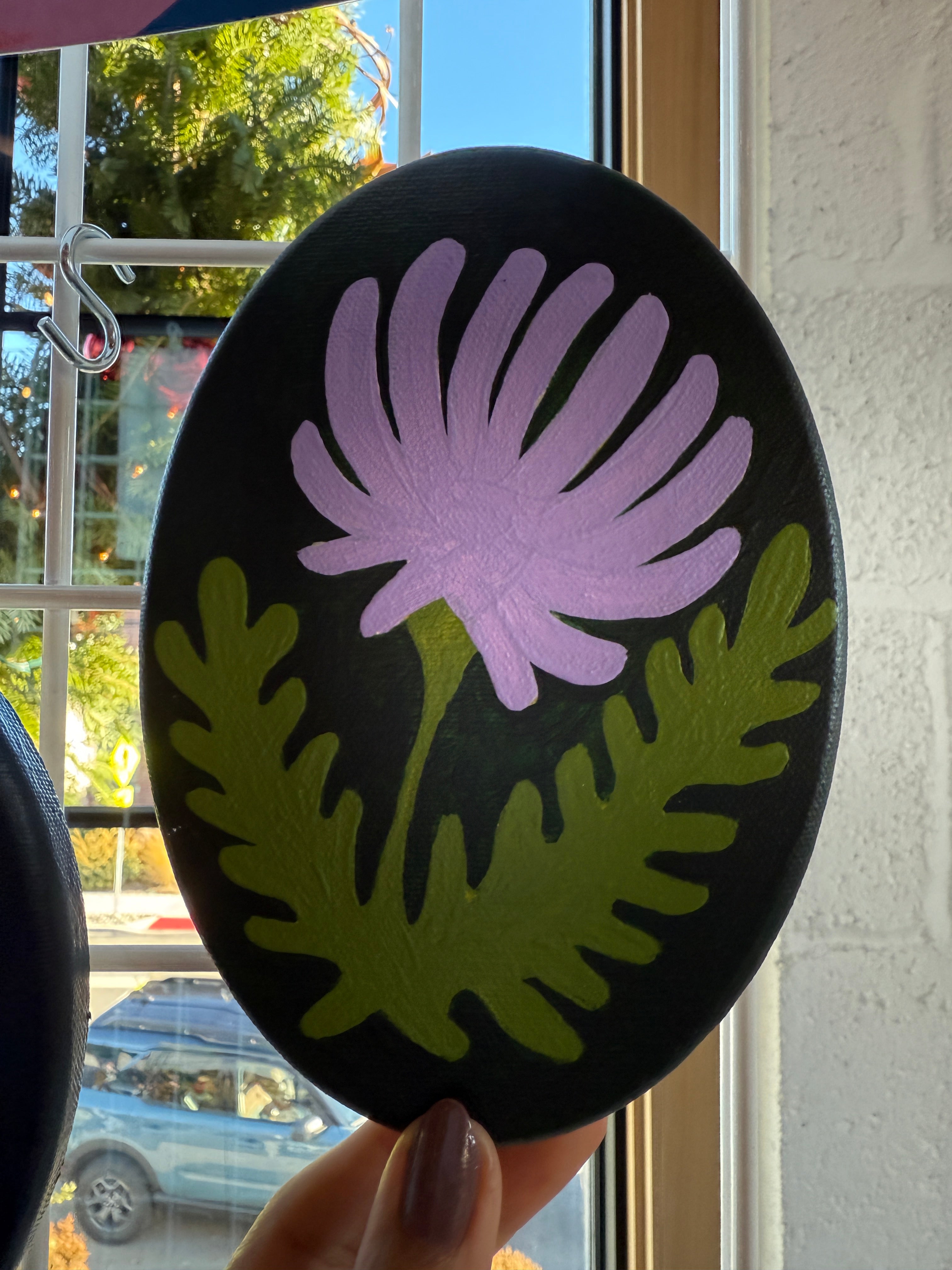 Round black coaster with purple flower and green leaves design held by a hand.